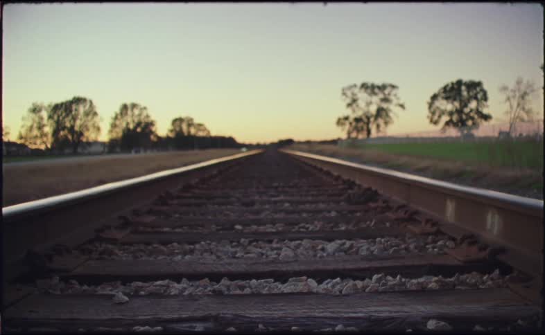 A few cars drive down a rural highway that parallels train tracks at dusk