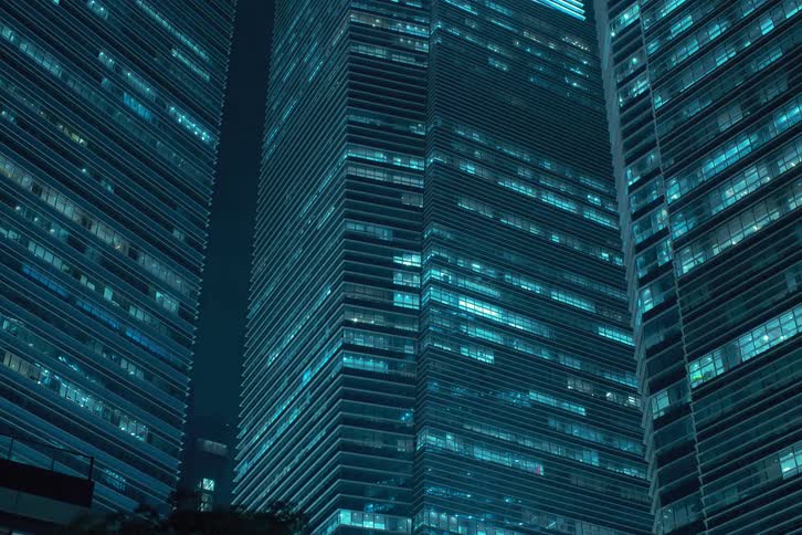 A cluster of towering skyscrapers illuminated with a cool blue light creating a striking contrast against the dark night sky