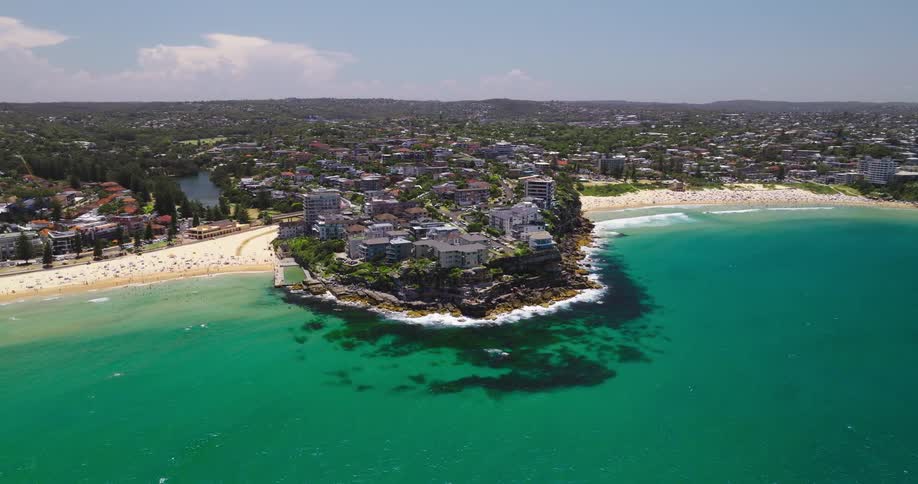 Aerial view of the coastline of sydney australia with the iconic manly beach stretching along the turquoise waters backed by lush green hills and dotted with buildings
