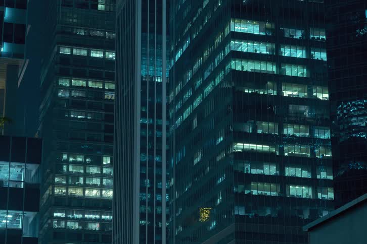 Nighttime view of a modern office building with numerous illuminated windows shutting down and turning off at the end of the day