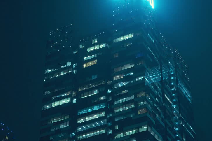 A clip looking up at a high rise building at night as time passes with windows flickering and blinking