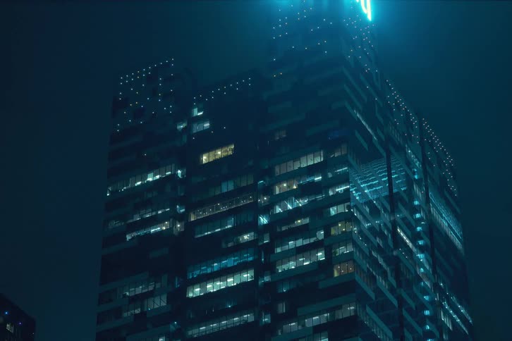 Nighttime view of a modern office building with numerous illuminated windows blinking at the end of the day