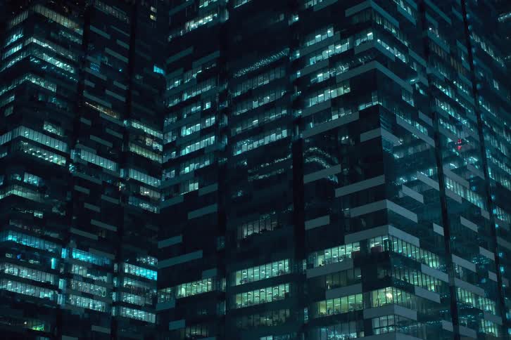 The windows of a skyscraper illuminate in a flickering pattern at night creating a dynamic gridlike effect on the facade