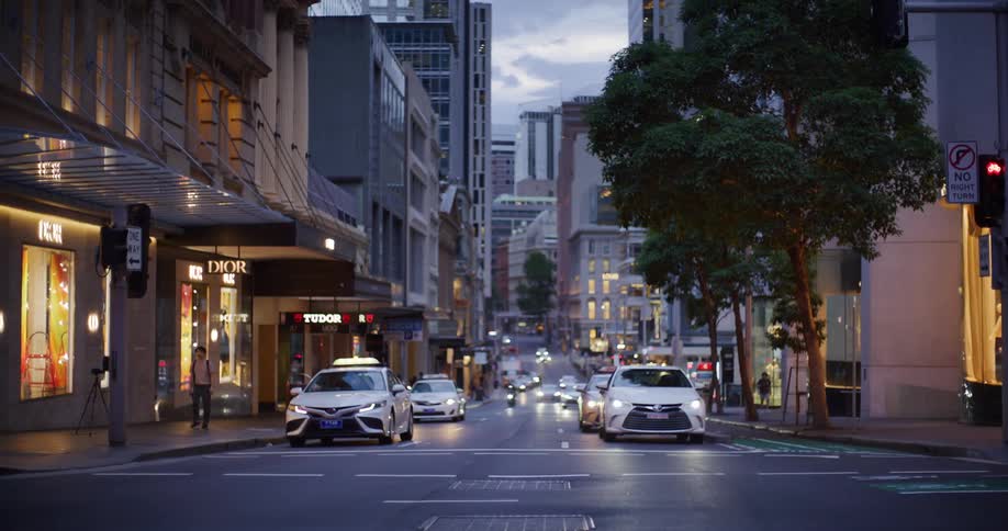 An urban street scene at dusk with several cars driving along the road