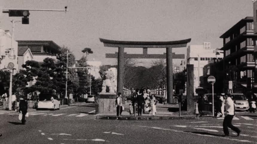 A busy street scene with pedestrians crossing the road near a large traditional japanese torii gate