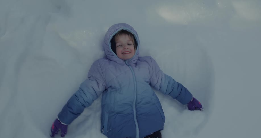 Little girl flapping her hands in the shape of wings while lying in the snow and playing