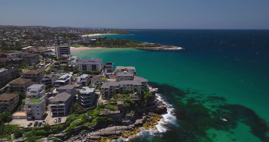 A coastal scene with a rocky outcrop featuring several buildings surrounded by turquoise waters and sandy beaches