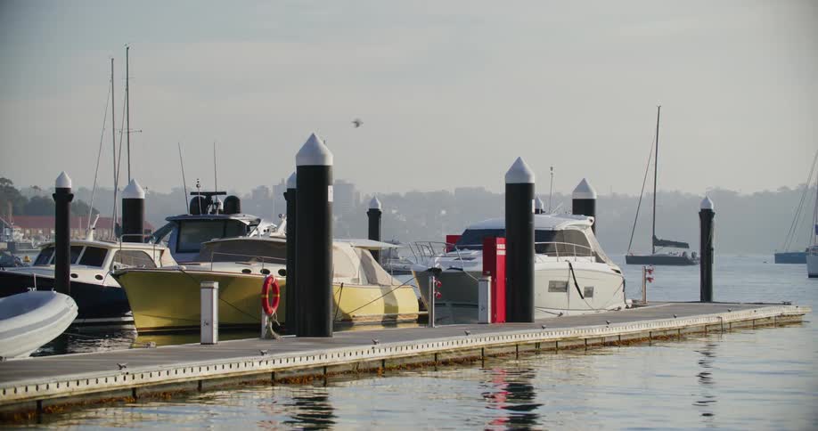 A marina with several boats docked at a floating dock with mooring bollards and a fuel pump visible