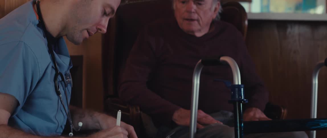 Nurse taking notes on a clipboard while sitting next to an elderly gentleman