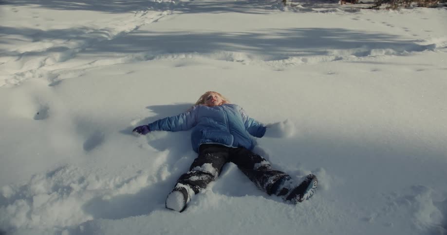 A girl is doing snow angels on the ground