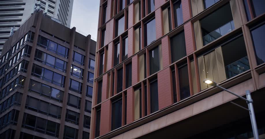 A modern high rise building with a contrasting facade of dark glass and warm toned panels stands tall amidst other skyscrapers