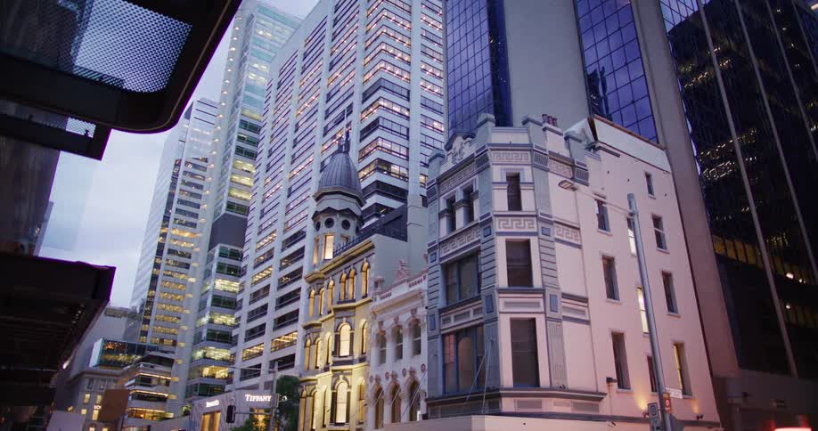 A vibrant city street at dusk where modern skyscrapers stand tall alongside historic buildings
