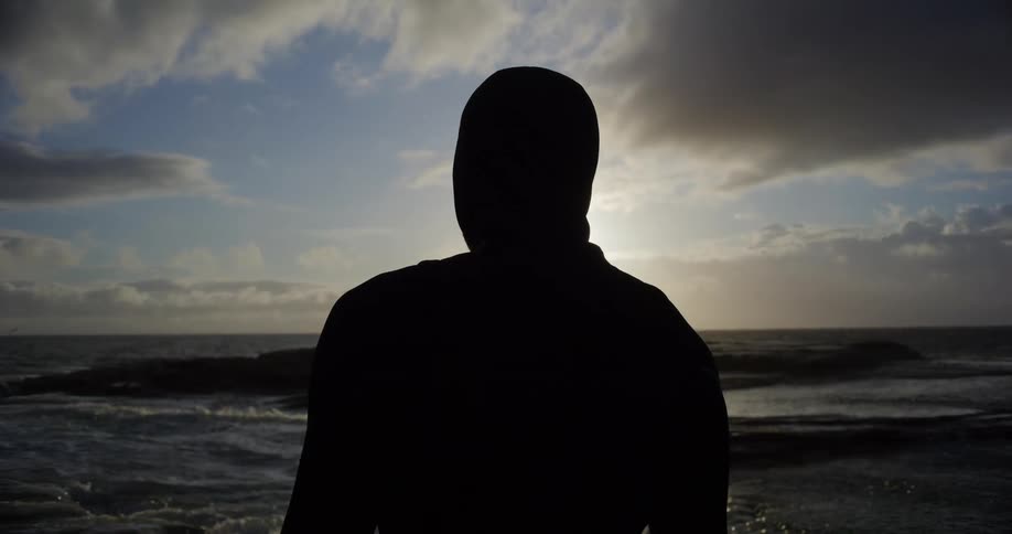 Silhouette of a man with his back turned and facing the sea at dawn
