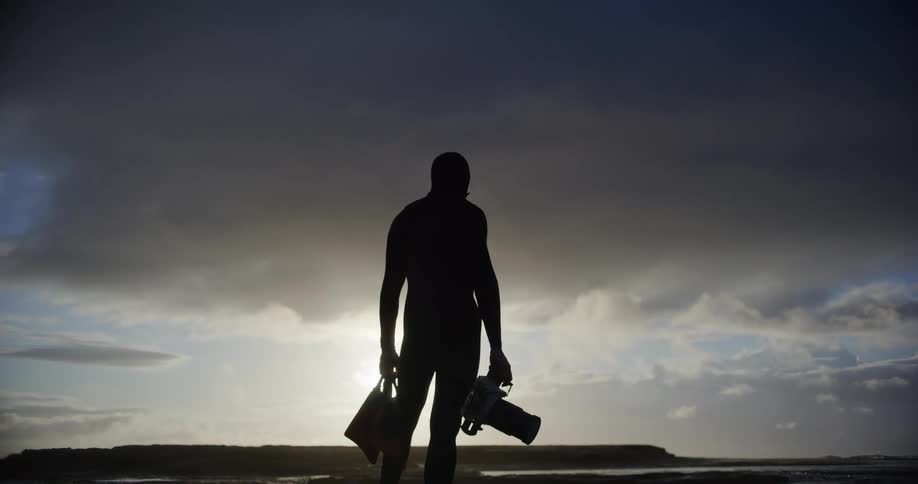 Silhouette of a filmmaker holding a professional camera in a backpack in a natural area
