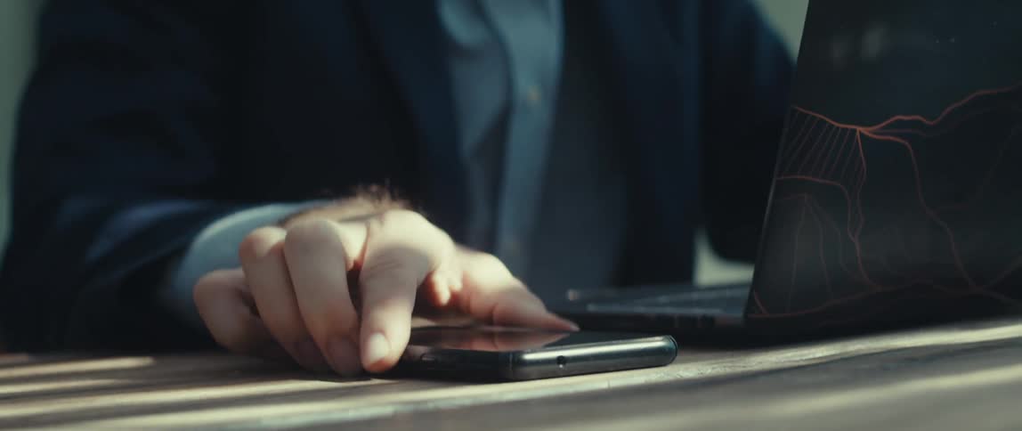Mans hand interacting with a laptop and looking at the smartphone next to it