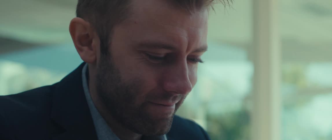 A man with blond hair is wearing a suit and looking to his side with his head in his hand and then he looks forward and smiles