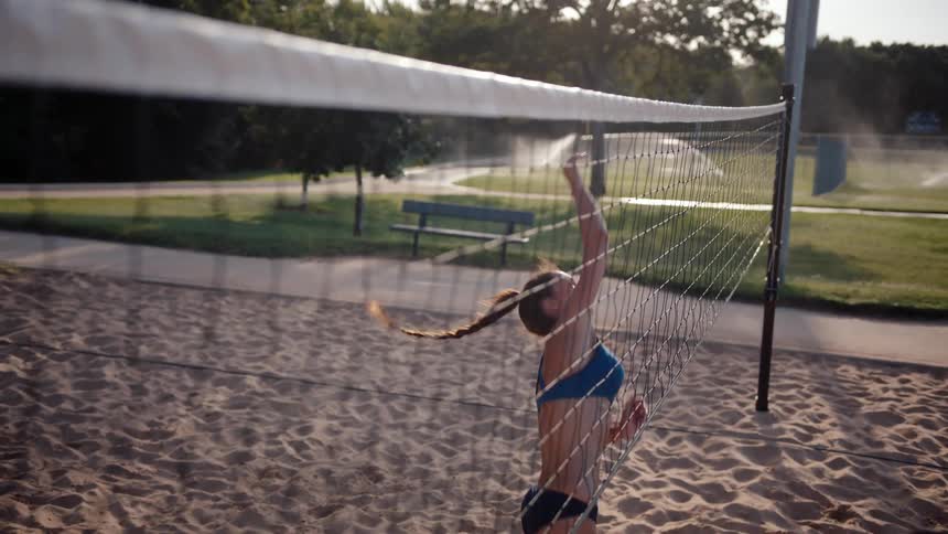 A woman playing sand volleyball jumps and hits the ball over the net