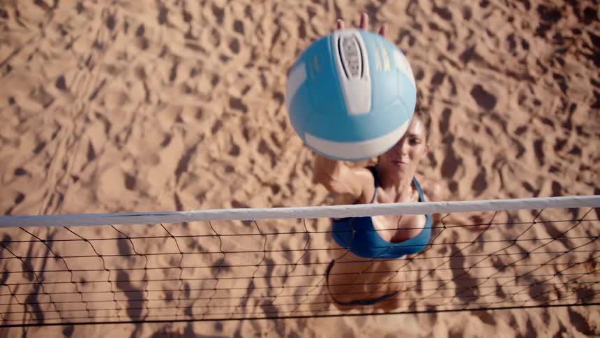 Woman jumping and throwing a volleyball on a sand court