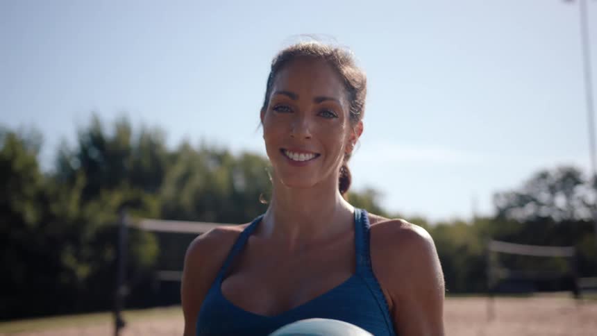 Portrait of a smiling woman holding a volleyball with a sand court in the background