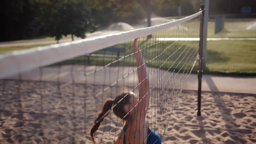 Woman on a sand court jumping and hitting a ball over the net playing volleyball