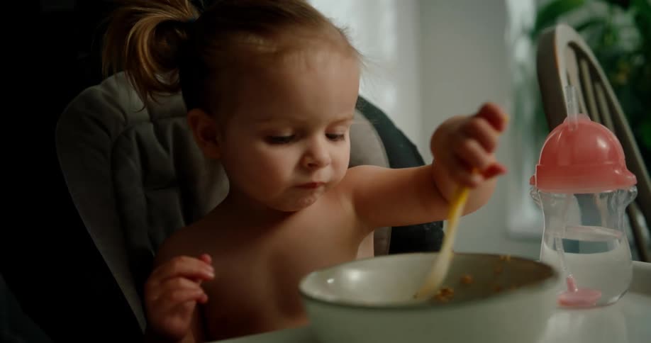 Toddler sits in high chair eating by herself
