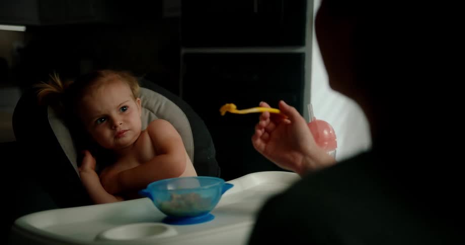 Toddler resists eating spoonful of food presented by her mother