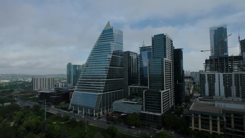 Modern cityscape with several skyscrapers highlighting a building with a sloping roof and glass facade