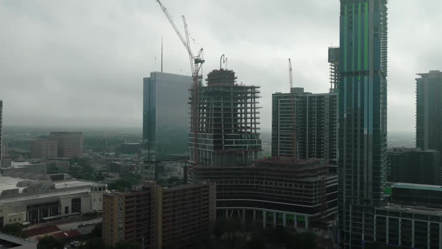Cityscape with multiple highrise buildings under construction cranes visible against the skyline and overcast weather conditions