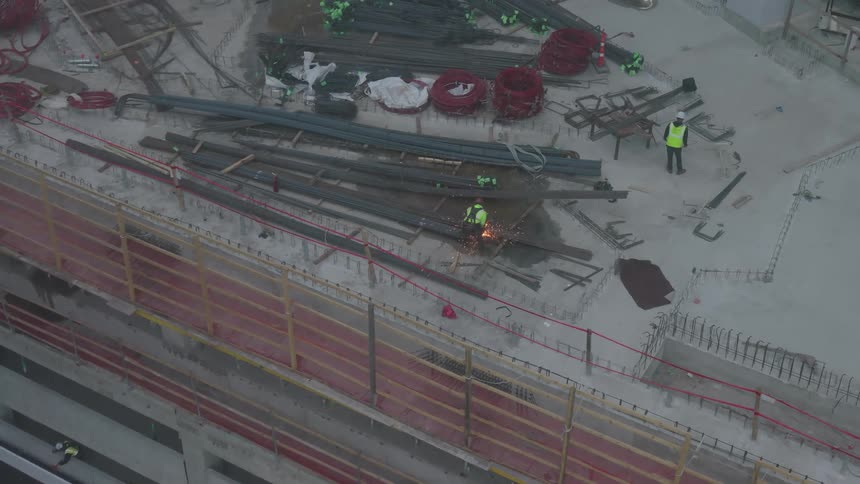 Two workers on top of a building under construction and one of them is welding and causing several sparks to rise upwards