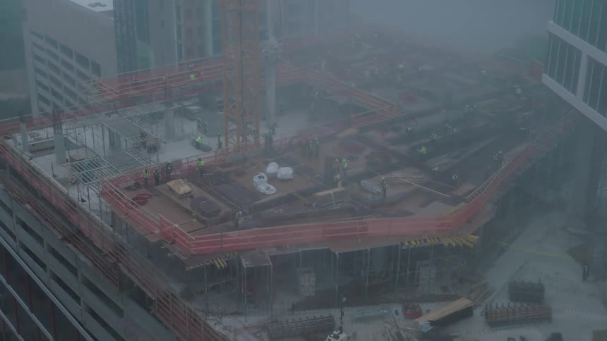 Some workers working on the construction of a building that is full of equipment and materials on top and there is a small fog hanging in the environment