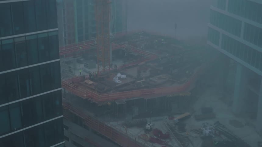 Dense fog shrouds building under construction between skyscrapers