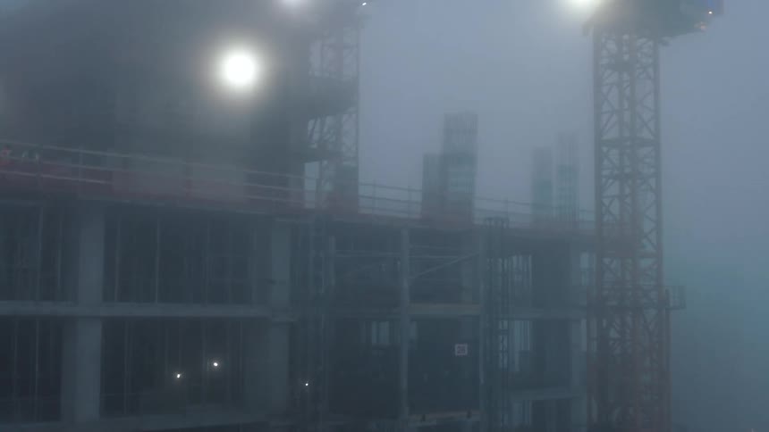 A large building under construction with a huge crane next to it and the whole environment is covered in thick fog
