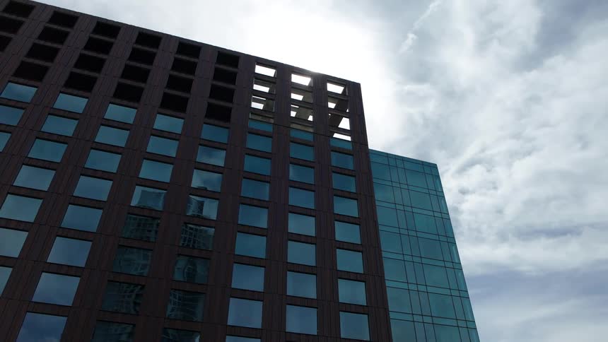 Upward view of a modern mirrored building against a blue sky with clouds