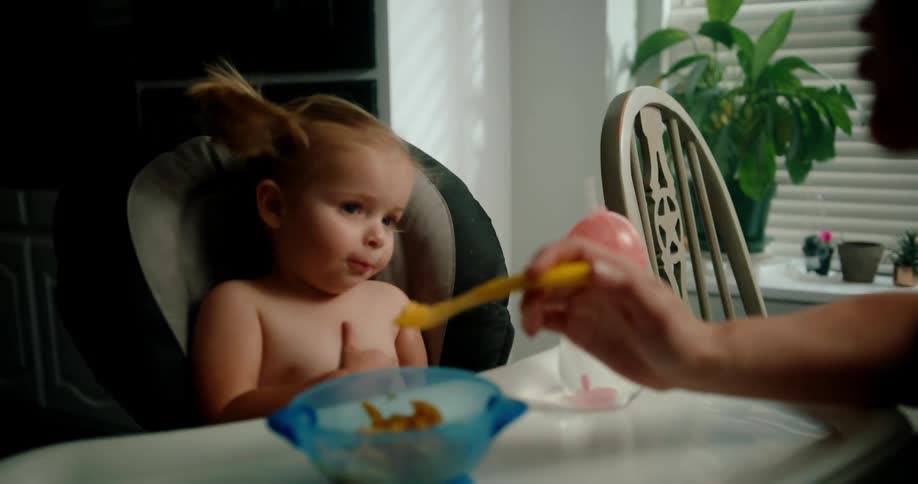 Girl sitting in a high chair watching someone offer her a spoonful of food
