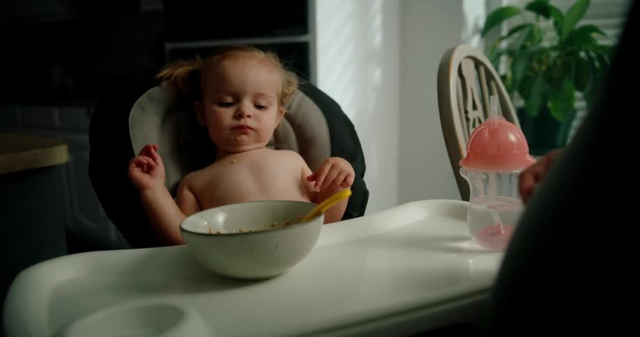 A person is feeding a child sitting in a high chair with a spoon