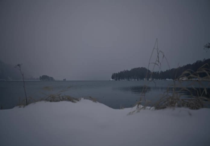Ice landscape in the foreground on the shore of a calm lake on a cloudy day