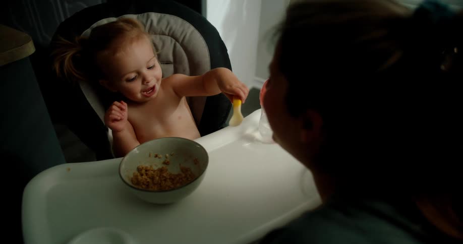 Little daughter sitting giving a spoonful of food to her mother