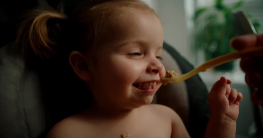Hand holding a plastic spoon and giving food to a happy little girl