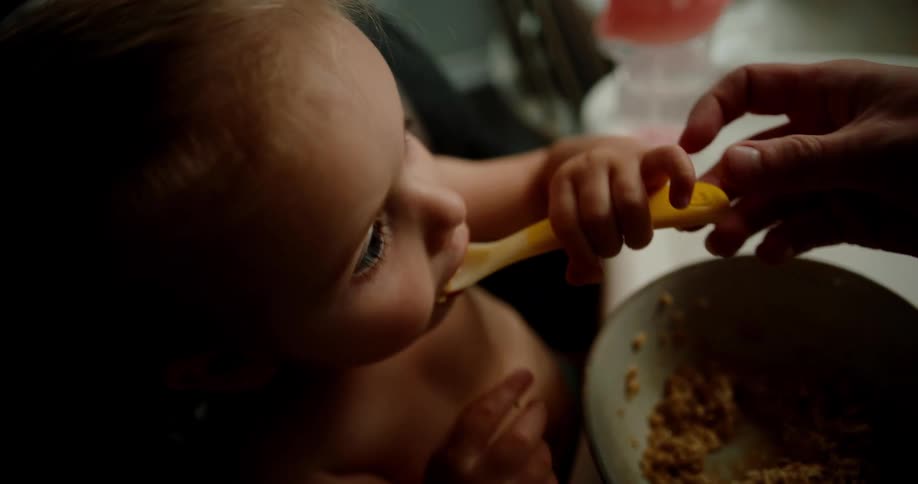 Little girl sitting with help from another person eating