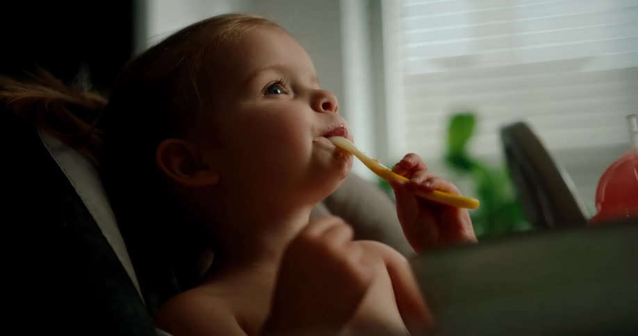 Portrait of a little girl sitting happily and holding a yellow plastic spoon