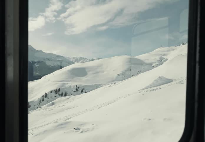 Cable car moving over the snow covered mountain slope looks out onto a mountain range under a cloudy sky