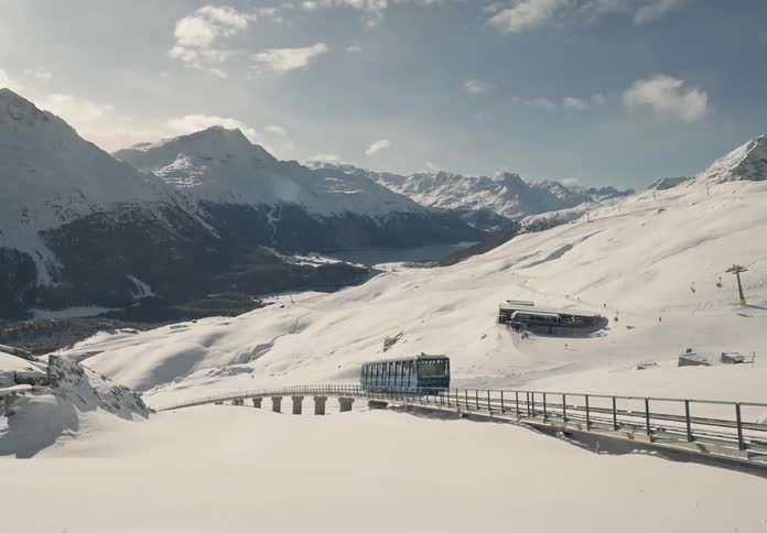 Train passing through a snowy mountain with people skiing and cable cars in the background