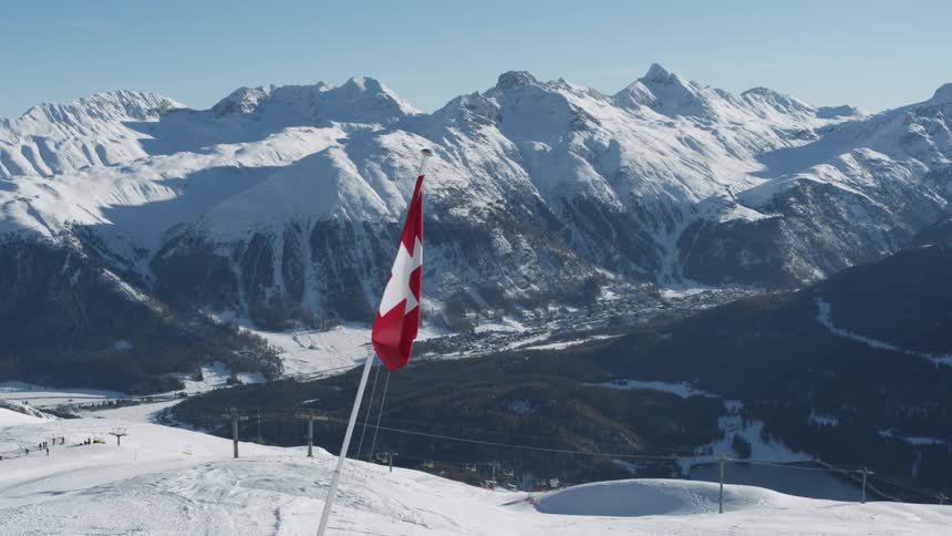 Swiss flag sits on a snowy slope while a ski lift operates near a valley in the mountains during a winter day