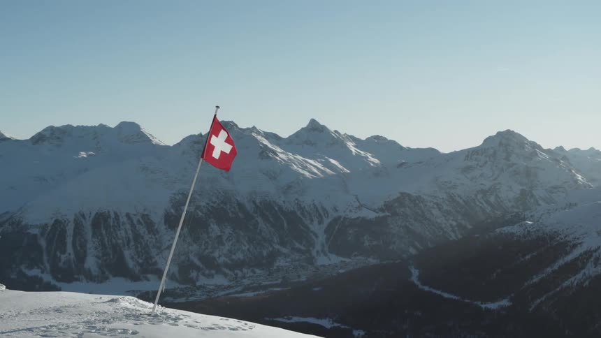 Swiss flag on a mountain surrounded by other snowy mountains seen during the day