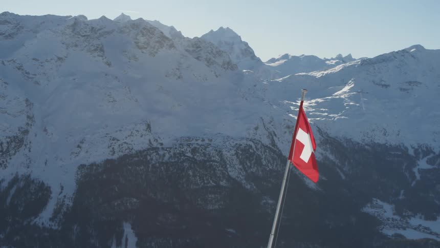 Swiss flag on a hill surrounded by snowy mountains