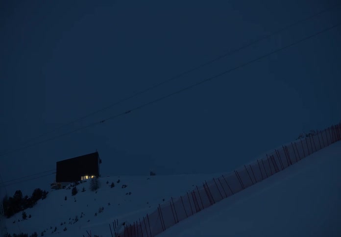 Snowy mountain at night and in the background an illuminated house
