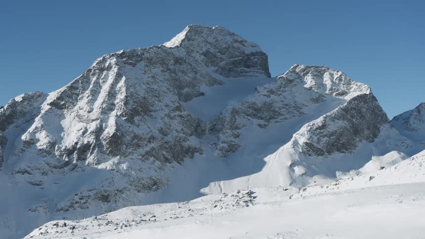 A snow capped mountain peak standing tall against a clear blue sky its rugged slopes and glacial ice