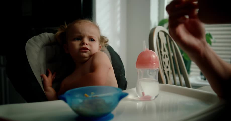 Mother eating food from her little daughter who is sitting in a highchair