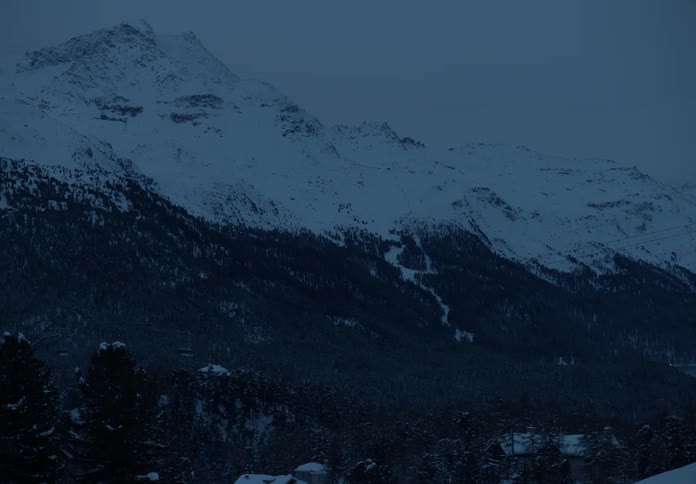 Snowy mountain landscape with conifers and a moving cable car at dusk