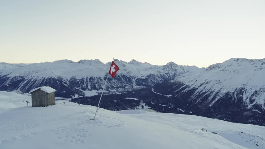 Panorama of a swiss flag on top of a mountain and in the background a cabin and ski lifts